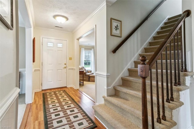 entryway with light wood-type flooring, visible vents, a textured ceiling, stairway, and crown molding