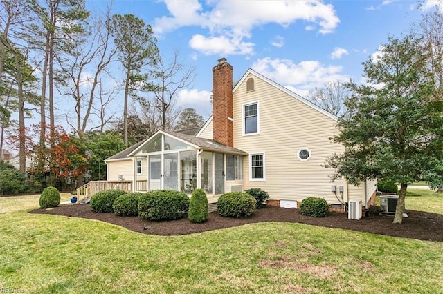 rear view of house with central air condition unit, a lawn, a chimney, and a sunroom