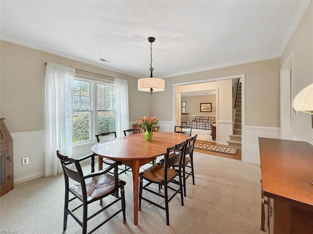 dining area with ornamental molding, light colored carpet, visible vents, and wainscoting