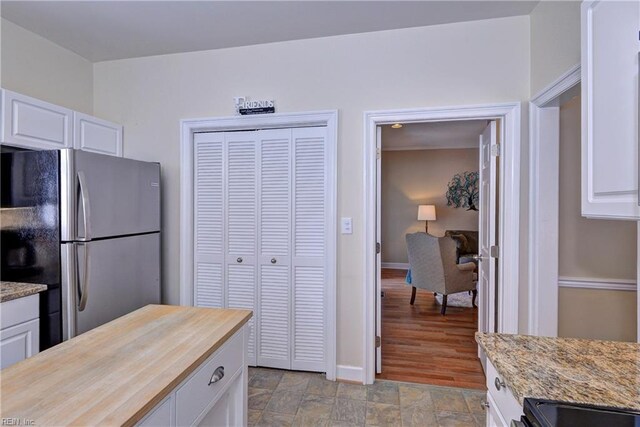 kitchen featuring light stone counters, stone finish floor, white cabinetry, and freestanding refrigerator