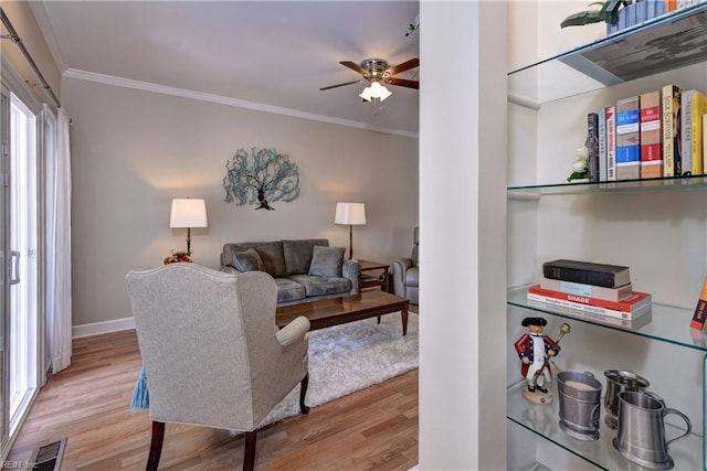 living room featuring baseboards, visible vents, light wood-style flooring, ceiling fan, and ornamental molding