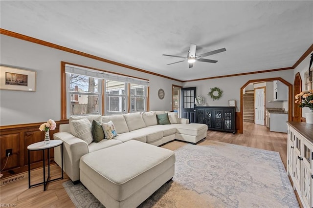 living area with a ceiling fan, visible vents, wainscoting, crown molding, and light wood-type flooring