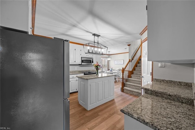 kitchen featuring a kitchen island, light wood-style flooring, white cabinets, appliances with stainless steel finishes, and decorative light fixtures