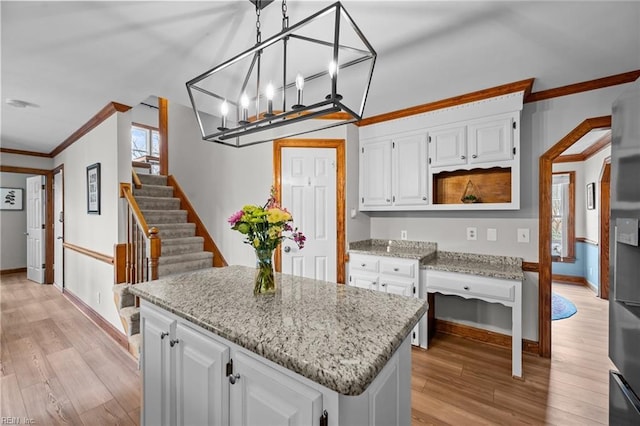 kitchen featuring light stone countertops, white cabinetry, ornamental molding, and light wood finished floors