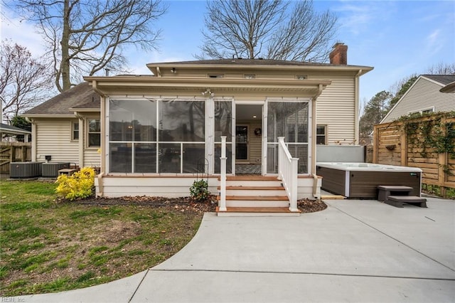 back of house featuring fence, a sunroom, a chimney, a hot tub, and a patio area