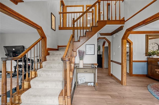 stairway featuring baseboards, arched walkways, a high ceiling, and wood finished floors