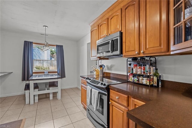 kitchen with dark countertops, stainless steel appliances, brown cabinetry, light tile patterned floors, and a chandelier