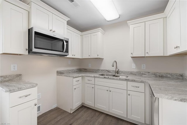 kitchen with stainless steel microwave, visible vents, dark wood-style floors, white cabinets, and a sink