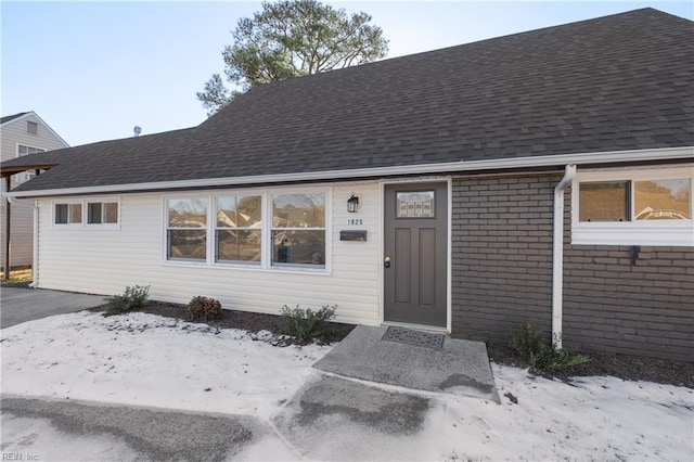 property entrance featuring brick siding and a shingled roof