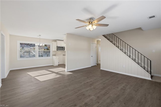 unfurnished living room with dark wood-style floors, stairway, ceiling fan with notable chandelier, and visible vents