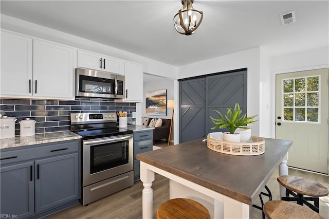 kitchen featuring visible vents, tasteful backsplash, wood finished floors, appliances with stainless steel finishes, and white cabinets