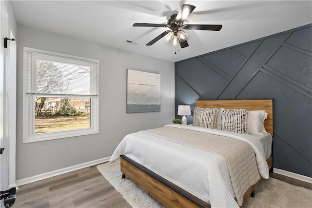 bedroom featuring visible vents, ceiling fan, baseboards, and wood finished floors