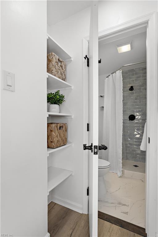 full bath featuring toilet, tiled shower, and wood finished floors