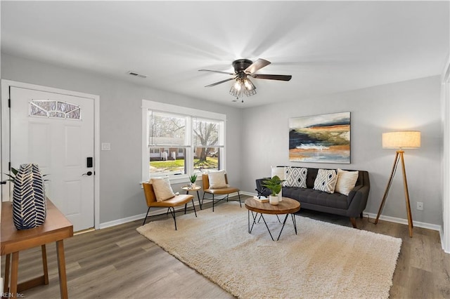 living room featuring visible vents, a ceiling fan, baseboards, and wood finished floors