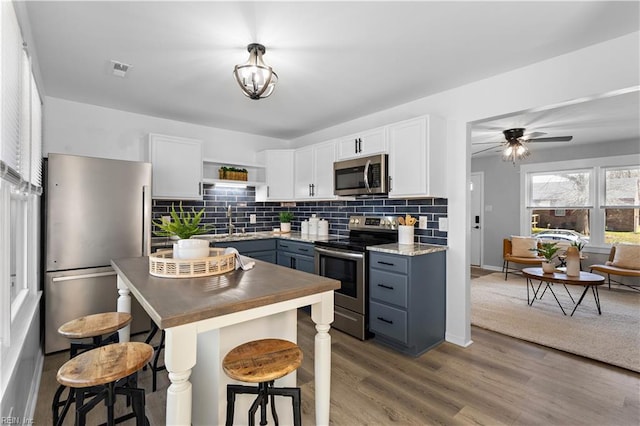 kitchen featuring backsplash, appliances with stainless steel finishes, wood finished floors, white cabinetry, and open shelves