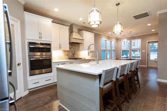 kitchen featuring tasteful backsplash, visible vents, custom exhaust hood, stainless steel appliances, and a sink