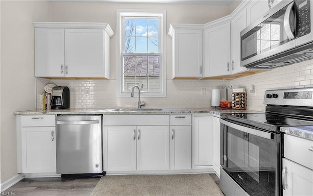 kitchen featuring a sink, light stone counters, stainless steel appliances, white cabinets, and decorative backsplash