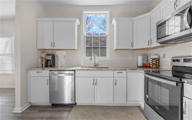 kitchen with light stone countertops, decorative backsplash, appliances with stainless steel finishes, white cabinets, and a sink