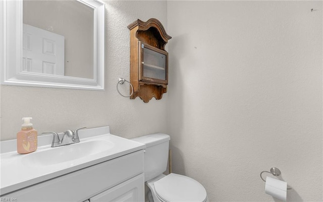 bathroom with toilet, vanity, and a textured wall