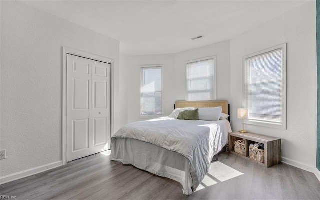 bedroom featuring visible vents, baseboards, wood finished floors, a textured wall, and a closet