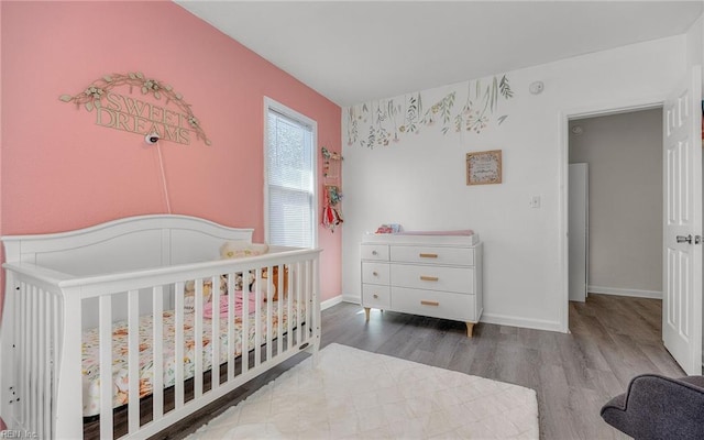 bedroom with a crib, baseboards, and wood finished floors