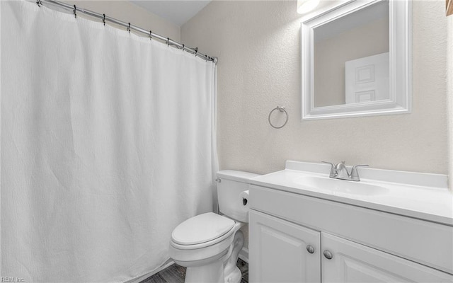 full bath featuring vanity, toilet, and a textured wall