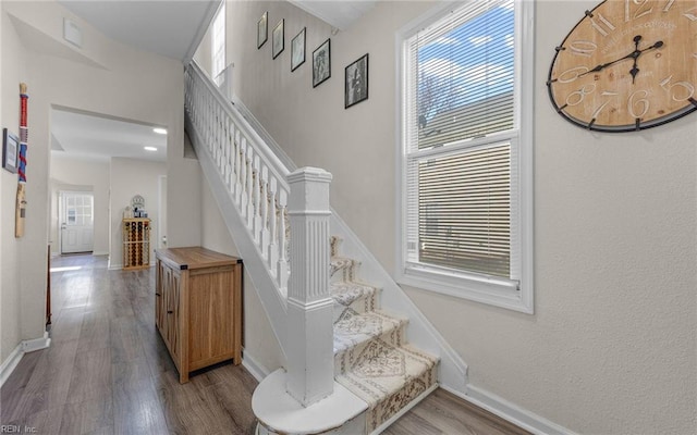 stairway featuring wood finished floors, baseboards, and a healthy amount of sunlight