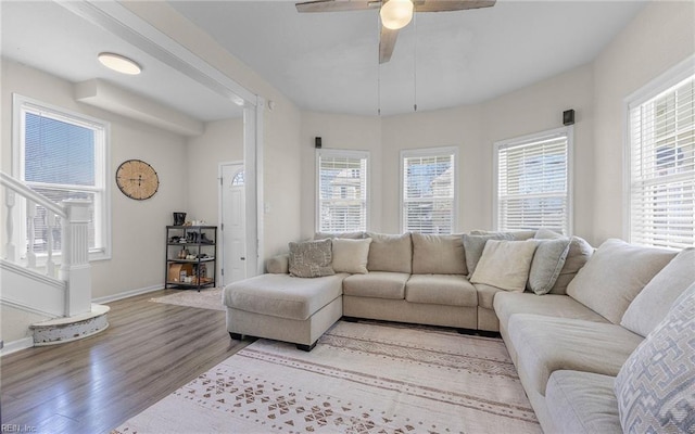 living area featuring stairs, baseboards, light wood finished floors, and ceiling fan