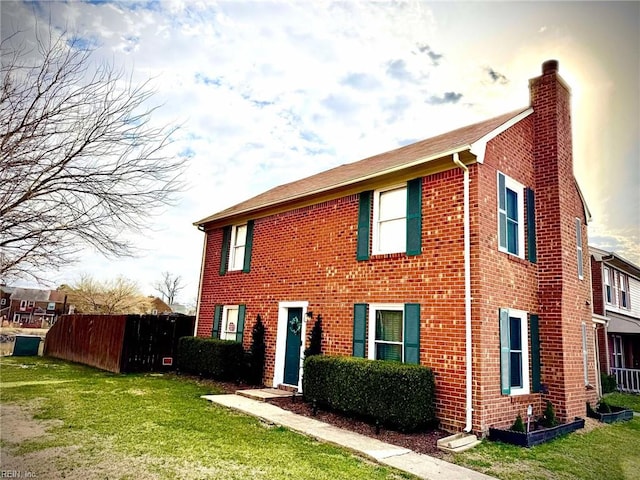 view of front of home featuring brick siding, a front lawn, a chimney, and fence