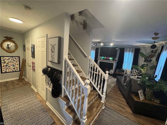 stairs featuring baseboards, a textured ceiling, wood finished floors, and a fireplace