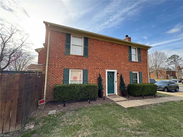 colonial inspired home with brick siding, a chimney, a front lawn, and fence