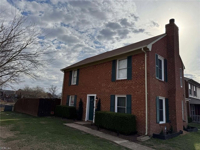 view of front facade featuring a front lawn, fence, brick siding, and a chimney