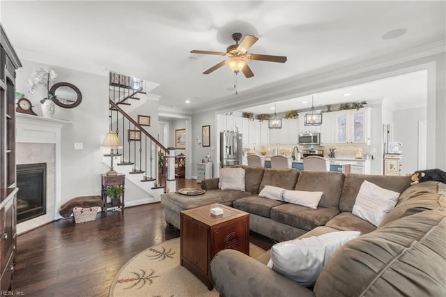 living room featuring wood finished floors, a ceiling fan, ornamental molding, stairs, and a tiled fireplace