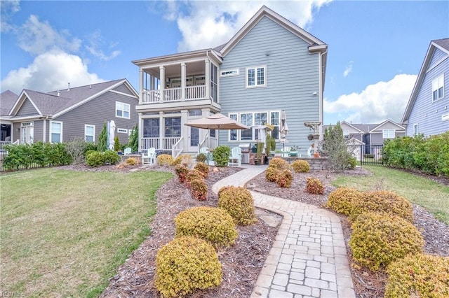 rear view of property featuring a balcony, a yard, and fence