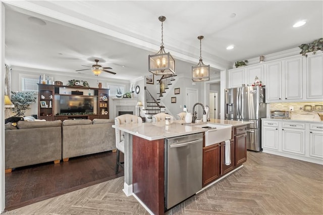 kitchen featuring tasteful backsplash, an island with sink, appliances with stainless steel finishes, a fireplace, and hanging light fixtures