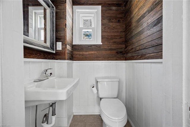 half bathroom featuring tile patterned flooring, toilet, wood walls, and a sink