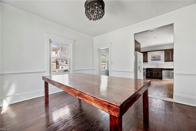 unfurnished dining area featuring dark wood finished floors, crown molding, and baseboards