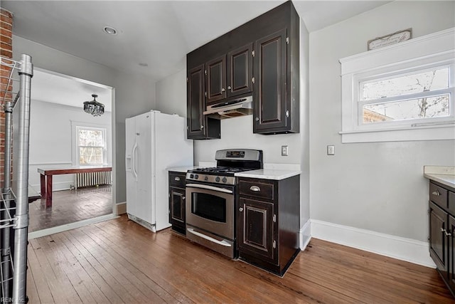 kitchen with dark wood-type flooring, under cabinet range hood, white fridge with ice dispenser, light countertops, and stainless steel range with gas stovetop