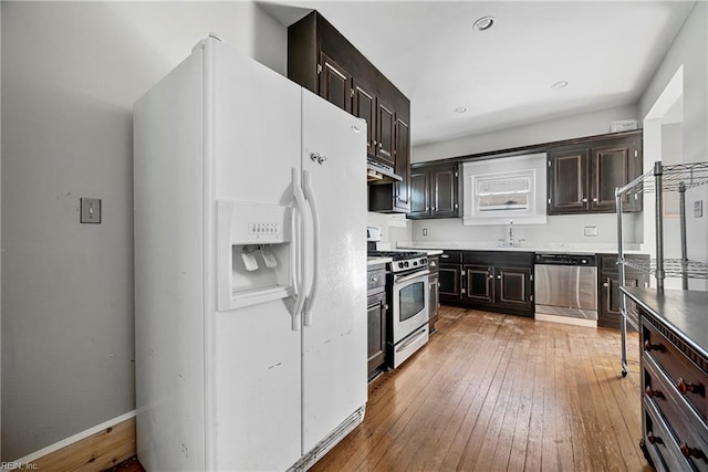 kitchen with light wood-type flooring, a sink, under cabinet range hood, appliances with stainless steel finishes, and dark brown cabinets