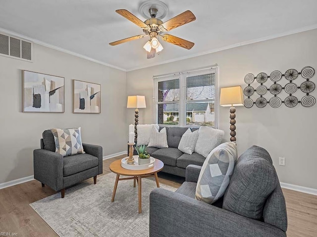 living area with visible vents, baseboards, crown molding, and light wood-style floors