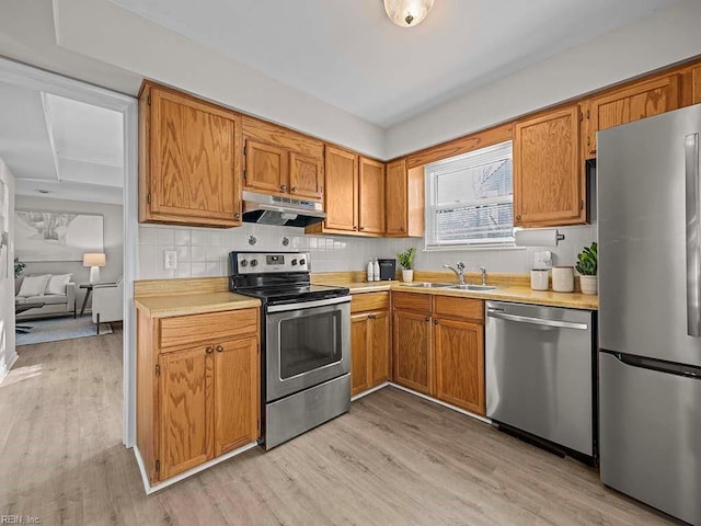 kitchen with a sink, light countertops, light wood-style floors, under cabinet range hood, and appliances with stainless steel finishes