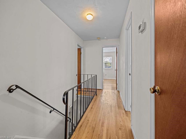 corridor featuring light wood-style flooring, an upstairs landing, and baseboards