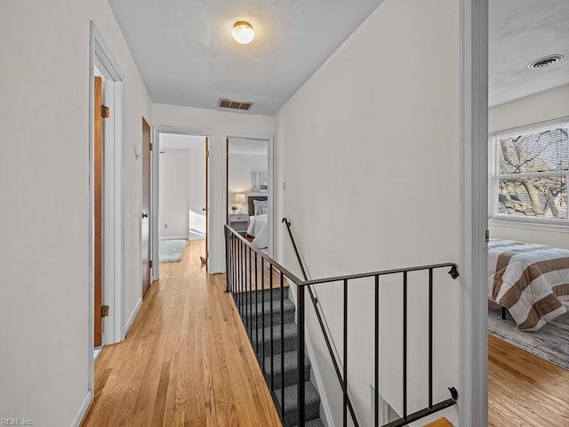 hallway with light wood-type flooring, visible vents, and an upstairs landing