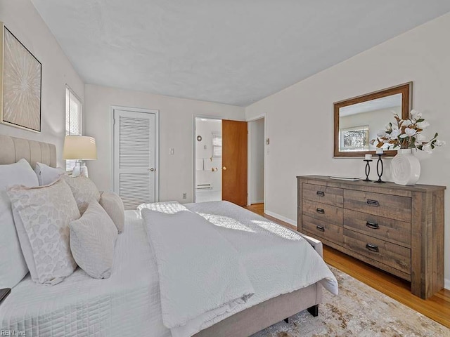 bedroom with a closet, light wood-style flooring, baseboards, and connected bathroom