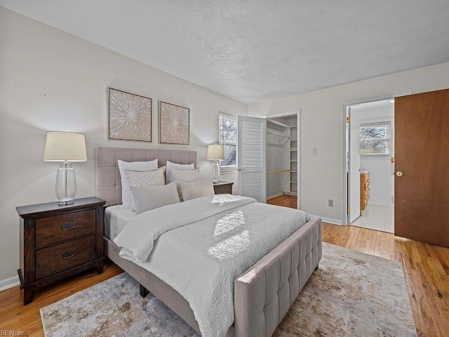 bedroom with a walk in closet, wood finished floors, baseboards, and a closet