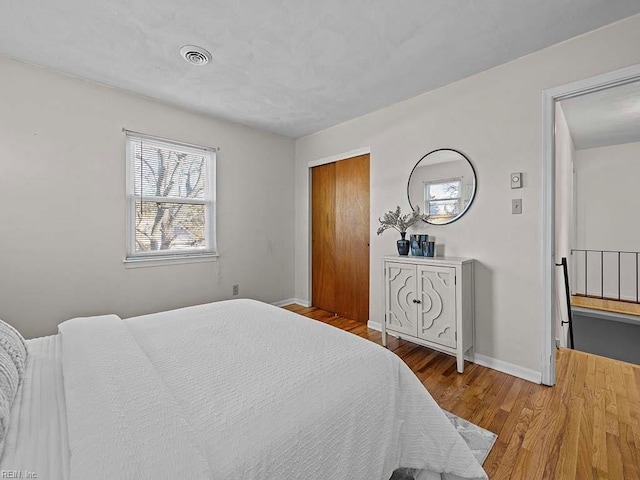 bedroom with a closet, visible vents, baseboards, and wood finished floors