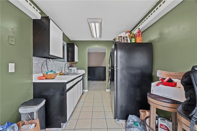 kitchen with light countertops, light tile patterned floors, decorative backsplash, freestanding refrigerator, and a sink