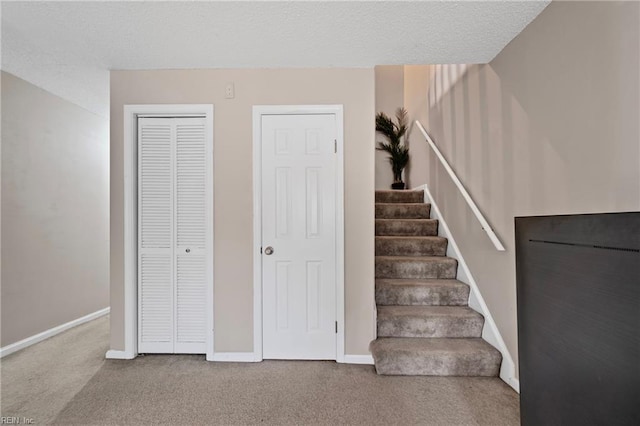 stairway featuring baseboards, a textured ceiling, and carpet flooring