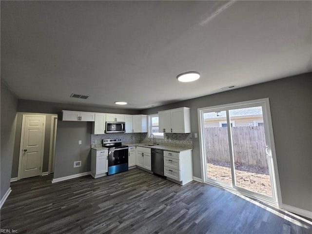 kitchen with visible vents, backsplash, stainless steel appliances, white cabinetry, and a sink