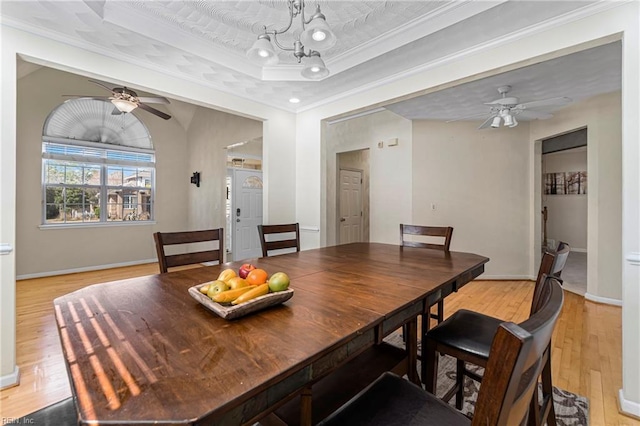 dining room with ceiling fan, a raised ceiling, light wood-style floors, and ornamental molding